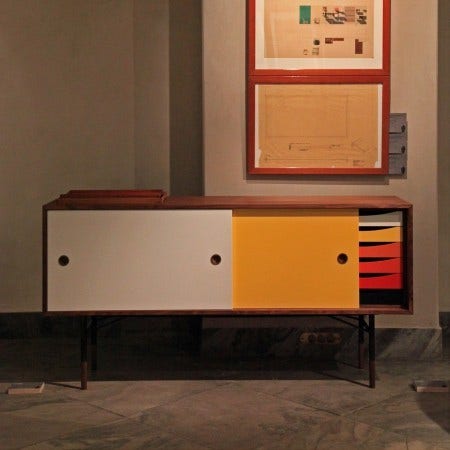 Finn Juhl was preoccupied with shapes and colors during his life because of his great interest in cubist and surrealistic art. The Finn Juhl Sideboard with colored sliding doors and trays was designed in 1955. It is part of a series of cubist wood cabinets that float on delicate steel frames with wood "feet".